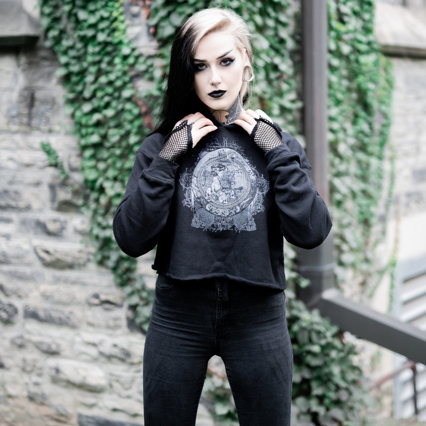 Goth model wearing the Eternal Echoes Graphic Crop Hoodie with Ouroboros and Divine Child design in a Victorian setting.