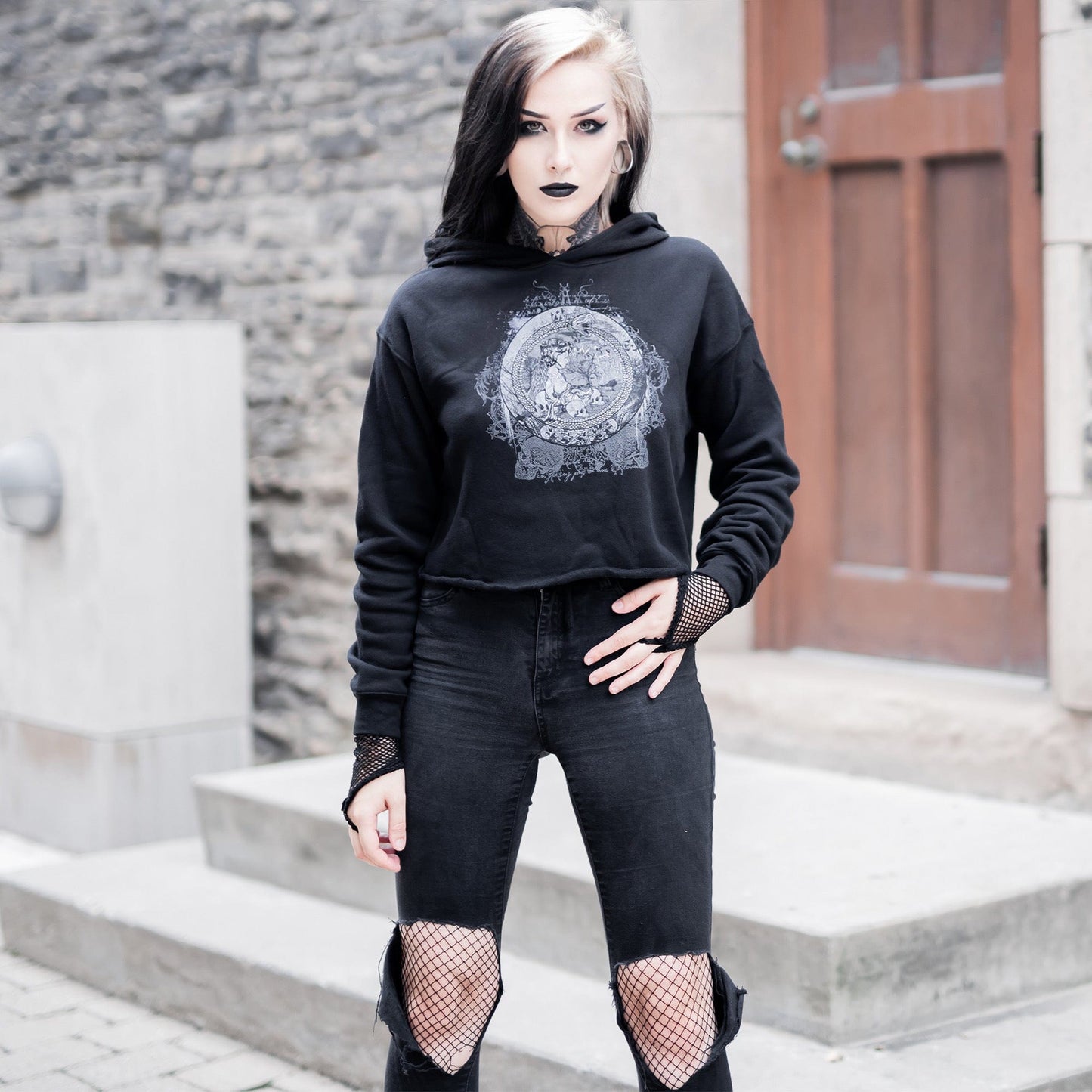 Goth model wearing the Eternal Echoes Graphic Crop Hoodie with Ouroboros and Divine Child design in a Victorian setting.