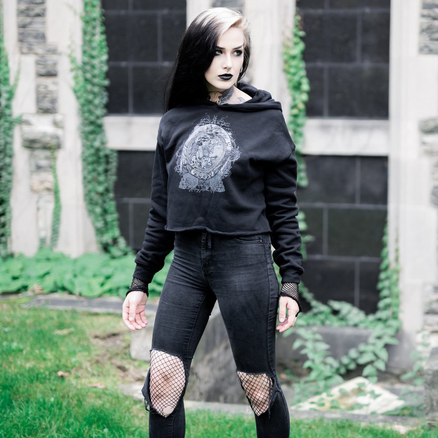Goth model wearing the Eternal Echoes Graphic Crop Hoodie with Ouroboros and Divine Child design in a Victorian setting.